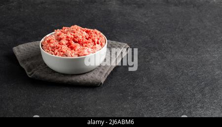 Assiette avec bœuf haché frais, textile sur fond gris noir, espace pour le texte, photo Banque D'Images