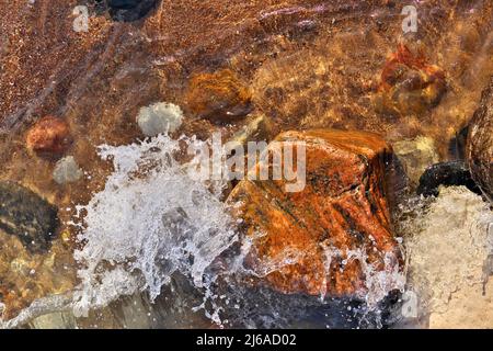 Directement au-dessus de la photo de petites vagues qui se roulent dans la plage parsemée de rochers et de Boulders colorés Banque D'Images