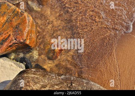 Directement au-dessus de la photo de petites vagues qui se roulent dans la plage parsemée de rochers et de Boulders colorés Banque D'Images