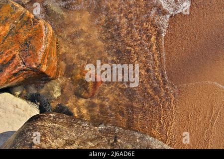 Directement au-dessus de la photo de petites vagues qui se roulent dans la plage parsemée de rochers et de Boulders colorés Banque D'Images