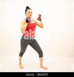 Belle femme blanche en rouge et gris sportswear, debout s'exerçant tenant un haltères, sur fond blanc. Banque D'Images