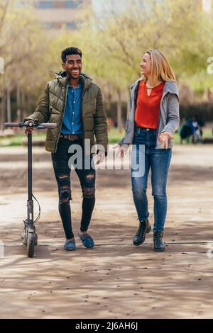 couple multiethnique parlant en marchant, il porte un scooter électrique Banque D'Images