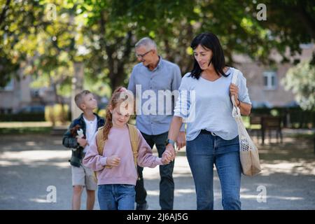 Des grands-parents heureux qui racontent leurs petits-enfants de l'école, qui marchent à l'extérieur dans la rue. Banque D'Images