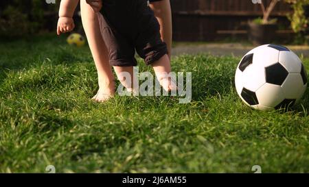 Bébé fait ses premiers pas sur l'herbe verte. Joyeux jeune mère joyeuse avec adorable bébé jouant à l'extérieur avec l'amour dans le jardin d'arrière-cour. Petit Banque D'Images