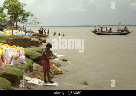 Les travailleurs se nettoient sur la rive de la rivière Rupnarayan avant le déjeuner pendant un projet de contrôle de l'érosion de la rivière, comme un bateau de traversée de rivière transportant des passagers arrive en arrière-plan à Tamluk, Purba Medinipur, Bengale-Occidental, Inde. Banque D'Images