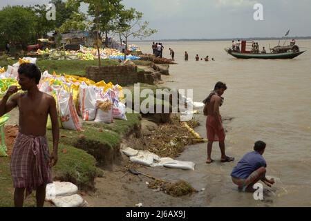Les travailleurs se nettoient sur la rive de la rivière Rupnarayan avant le déjeuner pendant un projet de contrôle de l'érosion de la rivière, comme un bateau de traversée de rivière transportant des passagers arrive en arrière-plan à Tamluk, Purba Medinipur, Bengale-Occidental, Inde. Banque D'Images