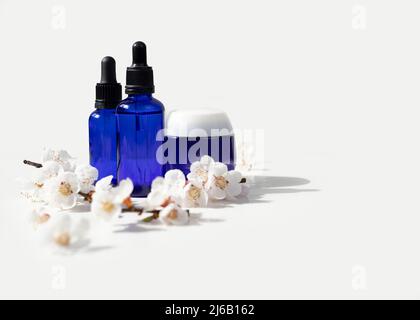 Flacons compte-gouttes en verre bleu avec couvercle noir et branche à fleur de cerisier sur fond blanc. Fond de source naturel. Produits de spa. Cosmétique biologique, bio et naturelle Banque D'Images