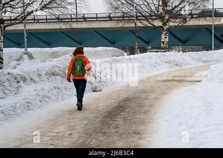 Une femme marchant sur une route urbaine, recouverte de neige boueuse, à Rovaniemi, en Finlande. Banque D'Images