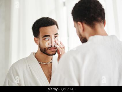 Jeune, beau et métasexuel regardant le miroir et appliquant des cellules oculaires sur son visage Banque D'Images