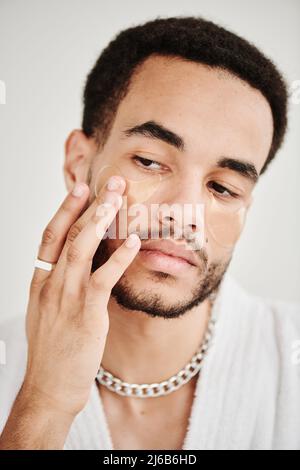 Portrait d'un jeune beau homme qui élève sa peau sous les yeux avec des taches oculaires Banque D'Images