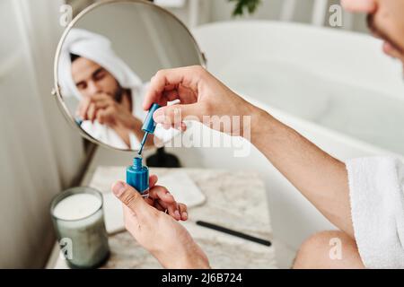 Gros plan du jeune homme ouvrant le vernis bleu et peignant ses ongles après la procédure de bain Banque D'Images