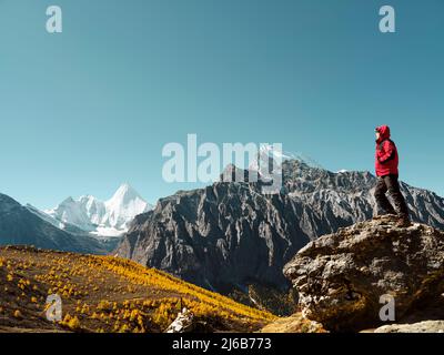 Homme asiatique debout sur le rocher regardant le sommet de la montagne de Yangmaiyong (ou Jampayang en tibétain) au loin à Yading, dans le comté de Daocheng, dans le Sichuan Banque D'Images