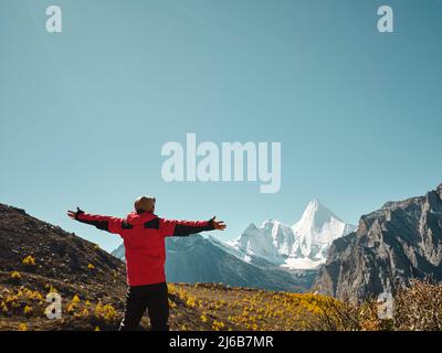 Vue arrière de l'homme asiatique se tenant au-dessus d'une montagne voisine, qui donne sur le mont Yangmaiyong (ou Jampayang en tibétain) avec des bras ouverts à Yading, Daocheng Banque D'Images