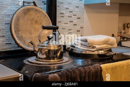 Une bouilloire en métal et des serviettes séchant sur une vieille cuisinière de cuisine le soir Banque D'Images