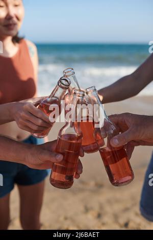 Gros plan sur des amis qui toaster avec des bouteilles en verre lorsqu'ils passent du temps à la plage Banque D'Images