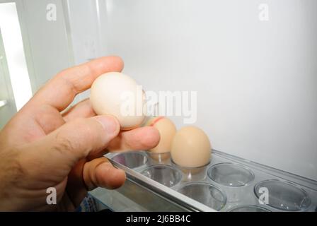 Main d'homme prenant l'œuf frais de la porte du réfrigérateur Banque D'Images