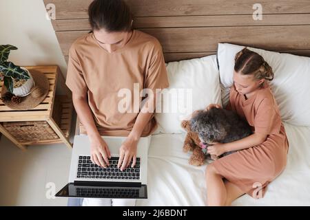Fille et petit chien regardant l'écran d'ordinateur portable de la mère qui travaille Banque D'Images