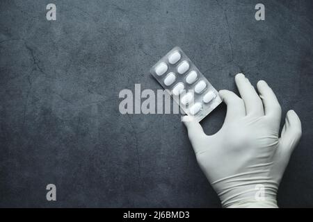 composition plate de la main dans des gants tenant un emballage blister sur fond noir Banque D'Images