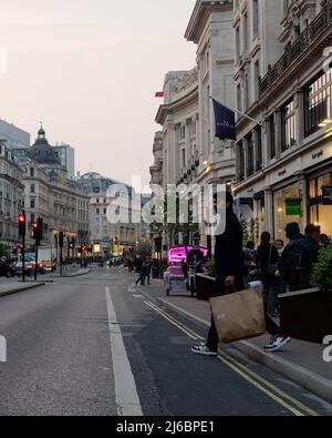 Londres, Grand Londres, Angleterre, avril 23 2022 : un homme avec un sac de shopping ordinaire traverse Regent Street dans la soirée avec un Rickshaw rose aka pedilab aka Banque D'Images