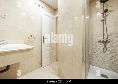 Salle de bains avec lavabo en porcelaine sur comptoir en marbre crème et cabine de douche intégrée avec porte en verre Banque D'Images