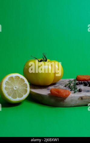 La tomate jaune, le citron, les grains de poivre, les feuilles de Laurier et les abricots séchés se trouvent sur une planche d'oliviers sur fond vert. Banque D'Images