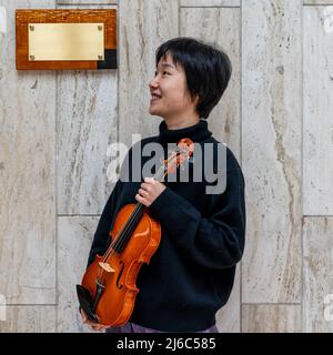 Jeune violoniste chinoise montrant son violon fraîchement préparé à l'extérieur devant son atelier Banque D'Images