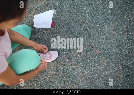 Vue aérienne d'une athlète féminine dans des vêtements de sport colorés nouant des lacets sur le terrain de sport, se préparer à l'entraînement en plein air Banque D'Images