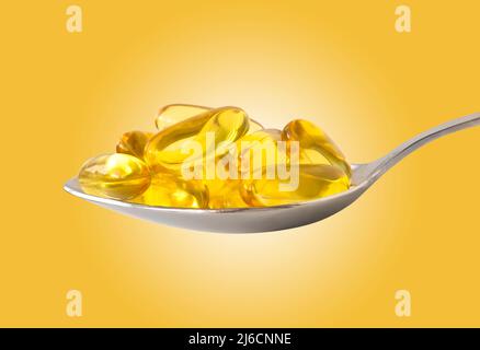Capsules d'huile de poisson Omega-3 dans une cuillère d'argent sur fond jaune Banque D'Images