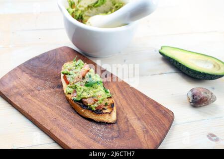 Guacamole sur une tranche de baguette, décor rustique avec des panneaux de bois, un mortier et un pilon Banque D'Images