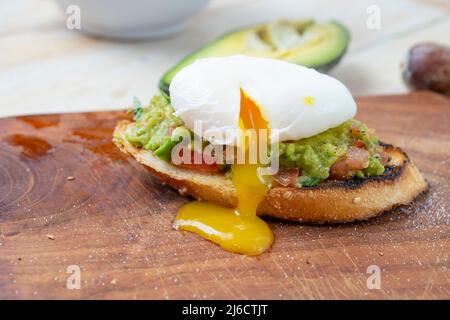 Œuf poché sur une tranche de pain grillé, avec guacamole et jaune goutte à goutte, gros plan sur une planche en bois Banque D'Images