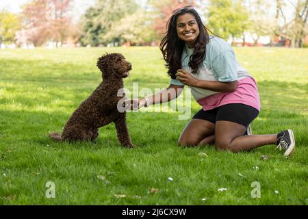 Une femme asiatique joue avec un chien chiot dans un parc de la ville. Jeune femme enseignant et chien d'entraînement à la poignée de main salutation Banque D'Images