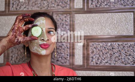 Une femme avec masque facial et concombre frais sur les yeux, se détendre à la maison. Portrait en gros plan de fille souriante dans un masque en argile. multani maison mitti visage pac Banque D'Images