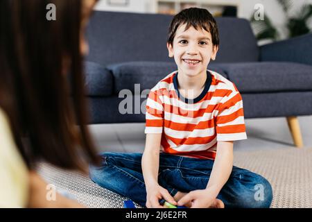 Joyeux garçon souriant à la caméra tout en jouant avec sa sœur à la maison. Banque D'Images