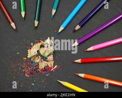 crayons de couleur aiguisés avec copeaux colorés sur fond d'ardoise noire, vue du dessus Banque D'Images