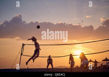 De jeunes amis jouant au volley-ball sur la plage au coucher du soleil Banque D'Images