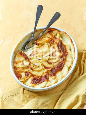bol de gratin de pommes de terre fraîchement cuit et serviette sur fond jaune Banque D'Images