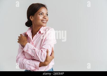 Jeune femme noire portant une chemise souriante tout en se serrant isolée sur fond blanc Banque D'Images