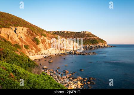 Les rochers colorés des montagnes de la table dans la baie de s'Abba Druche et la mer Méditerranée bleu profond dans la dernière lumière du coucher du soleil, la Sardaigne Banque D'Images