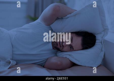 Guy dans le lit couvrant sa tête avec un oreiller Banque D'Images