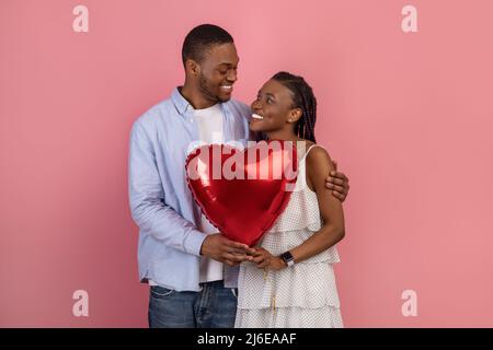 Jeune couple noir romantique qui enserre et tient une montgolfière en forme de coeur Banque D'Images