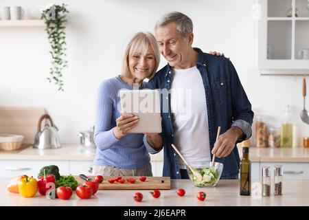 Un couple senior lit la recette sur une tablette numérique dans la cuisine Banque D'Images