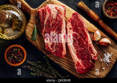 Vue de dessus viande crue bœuf marbré. Sur une planche à découper en bois, nappez les ustensiles de cuisine et les assaisonnements Banque D'Images