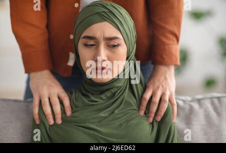 Un mari musulman méconnaissable touche les épaules d'une femme malheureuse à l'intérieur Banque D'Images