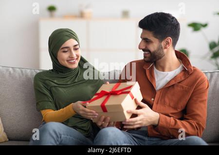 Joyeux homme musulman qui donne un cadeau à sa femme pour fêter ses vacances à l'intérieur Banque D'Images