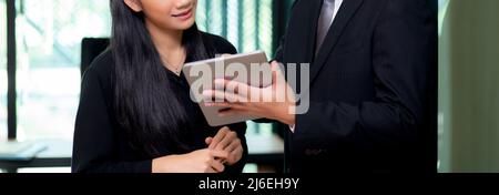 Jeune homme et femme d'affaires asiatique debout et parlant de marketing sur tablette avec le réseau social au bureau, rapport de secrétaire avec le bourreau Banque D'Images