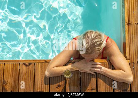 Vue de dessus d'une femme mouillée debout dans la piscine et penchée sur un bord de bois. Banque D'Images