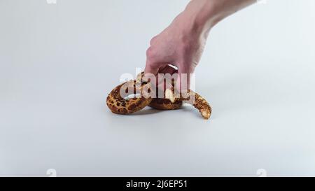 Une femme tient des anneaux de sésame turc traditionnels Kandil Simidi sur un fond blanc. Un anneau demi-mordu et deux petits pains entiers sont isolés. Banque D'Images