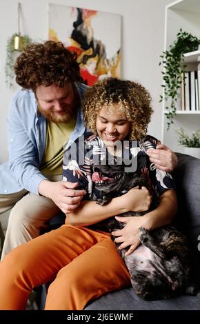 Couple multiethnique sans enfant obtenant un nouveau membre de leur famille, ils s'asseyant sur un canapé et liant avec le chien Banque D'Images