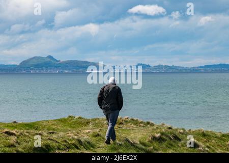 East Lothian, Écosse, Royaume-Uni, mai 1st 2022. Météo au Royaume-Uni : soleil sur la côte est de Lothian. Un homme senior marche le long de la côte Firth of Forth avec une vue sur la ville d'Édimbourg au loin Banque D'Images