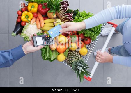 Femme qui paie des articles d'épicerie à l'aide de sa carte de crédit, la caissière du supermarché tient le terminal du PDV Banque D'Images